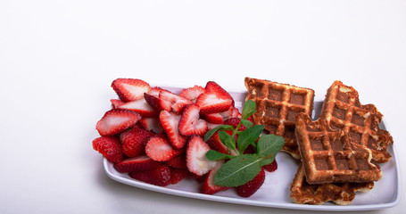 Freshly baked gluten free waffles with strawberries on mint  on a rectangular dish..
