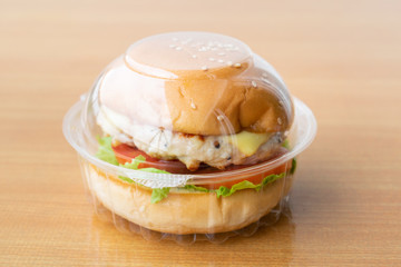 Chicken burger with cheese,lettuce and tomato in clear plastic box.