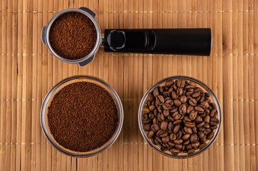 Holder from coffee maker with coffee, bowl with fried coffee beans, bowl with ground coffee on mat. Top view
