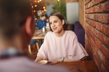 Gorgeous Caucasian brunette sitting in restaurant with her boyfriend and drinking coffee.