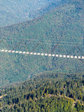 Suspension pedestrian bridge between high mountains above the forest. A helicopter flies over the green forest. View from the top.