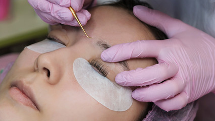 Eyelash extension procedure. Female eyes with long eyelashes. Cosmetic procedure in spa salon. Cosmetologist's hands in protective gloves are held with tweezers and false eyelashes.