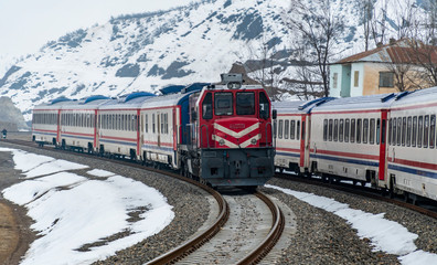Train at snow covered railway line in snowy valley between the mountains.