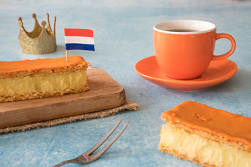 Orange tompouce, traditional Dutch treat with pudding and frosting on national holiday Kings Day (April 27th), in The Netherlands. With cup of coffee, crown and Dutch flag