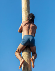 A man climbs a wooden pole against the blue sky