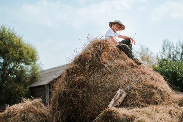 little boy sitting at the height of a large haystack in the village. The child the farmer.