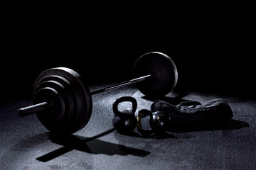 BACK LIT image of 365 pound weight on barbell with kettle bells and sand bag on gym floor