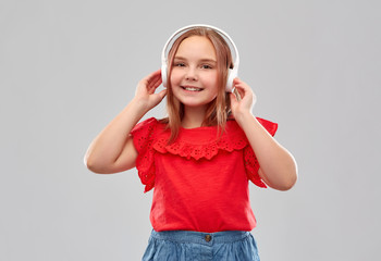 technology, audio equipment and childhood concept - beautiful smiling girl in headphones listening to music over grey background
