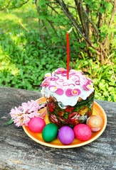 Easter cake with a candle, painted eggs, spring branches and flowers. Easter composition on the old wooden table.