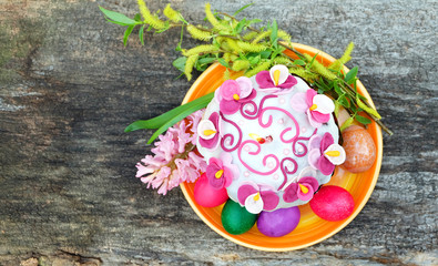 Easter cake with a candle, painted eggs, spring flowers. Easter composition on the old wooden table, top view.