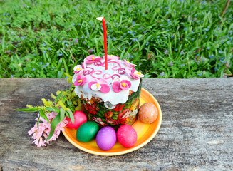 Easter cake with a candle, painted eggs, spring branches and flowers. Easter composition on the old wooden table.