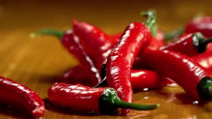 Red chili pepper pods slow motion falling under running water streams on rustic woode table in country style. Farm organic fresh products.