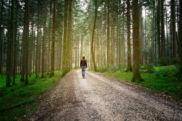 Man walks alone on forest road with mossy ground.