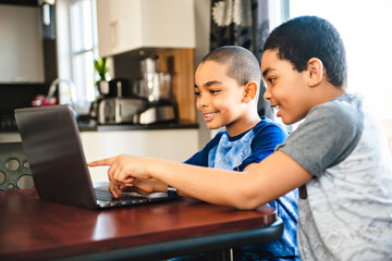 two Black boy sitting playing on a laptop computer at home