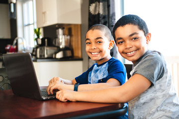 two Black boy sitting playing on a laptop computer at home