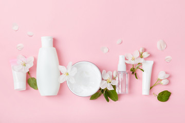 Face care products (tonic or lotion, serum, cream, micellar water, cotton pads, shaver) on pink background with spring apple blossom. Freshness natural anti-age care. Female everyday fresh cosmetics
