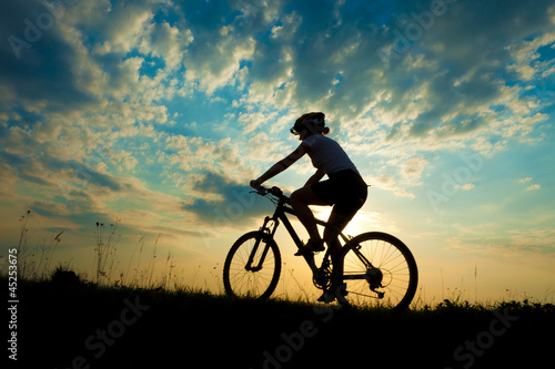  Biker-girl at the sunset on the meadow