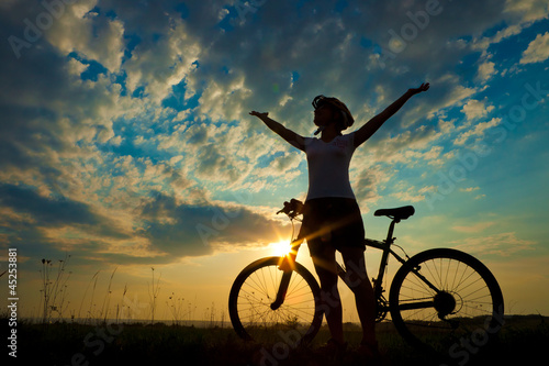 Fototapeta Biker-girl at the sunset on the meadow