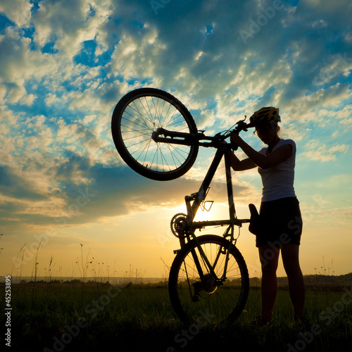 Fototapeta Biker-girl at the sunset on the meadow