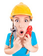 Surprised woman wearing a hardhat holding pliers and spanner