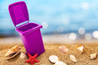Trash can on clean sand and shells with seascape background