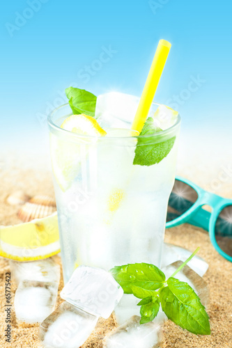  Cold water with lemon and ice on beach background