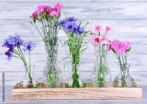  Beautiful summer flowers in vases on grey wooden background