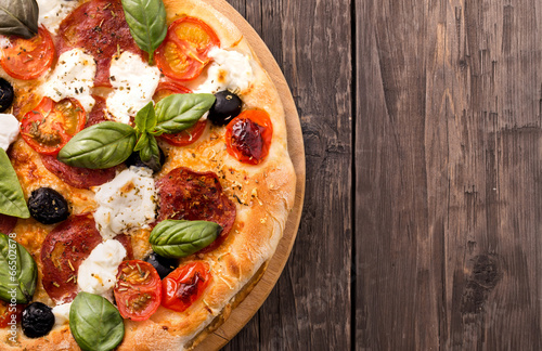 Poster Rustic pizza with salami, mozzarella, olives and basil on wooden