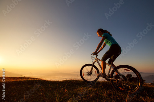 Fototapeta Biker-girl at the sunset on mountains