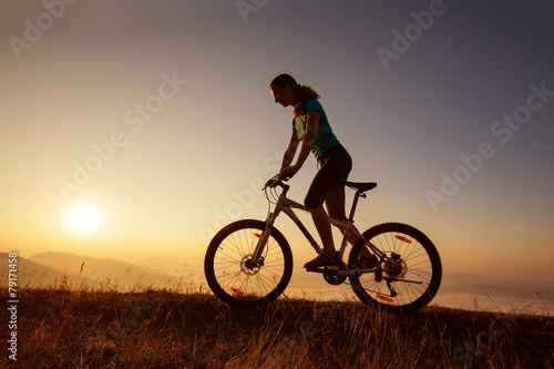 Fototapeta Biker-girl at the sunset on mountains