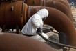Worker in protective equipment cleans the metal construction before painting them
