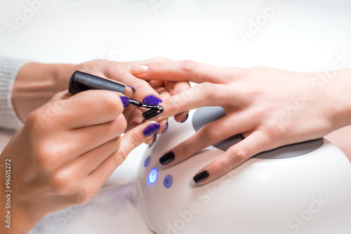 Zdjęcia Manicurist applies nail gel polish middle finger