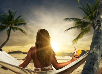 Young lady relaxing in hammock on the beach at sunset