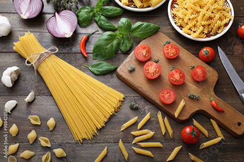 Poster vista dall'alto Pasta grezza con basilico e pomodoro su sfondo legno rustico