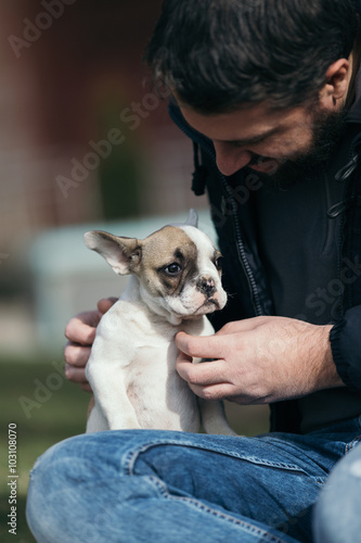 Handsome, bearded, middle age man enjoying outdoors with his adorable French bulldog puppy. City park in background. © tamara83