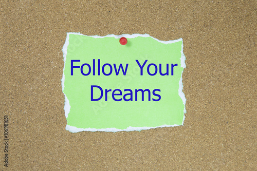 Poster The phrase follow your dreams in text on a green sticky note posted to a cork notice board