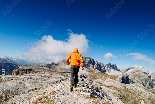 The guy in the orange jacket and sneakers running trails in the mountains. Dolomite, Alps