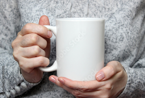 Girl is holding white cup in hands. White mug in woman's hands.