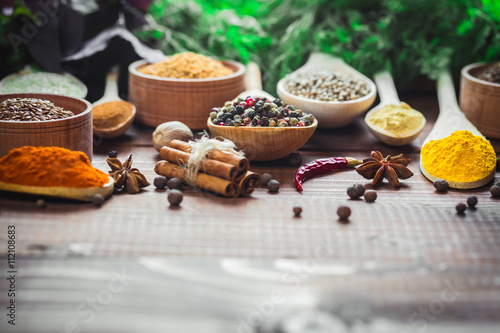 Beautiful colorful spices in wooden spoons and bowls with lettuce, dill and Basil on an old wooden brown table Poster