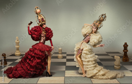Valokuva Battle of chess queens on chess board with chess figures on background