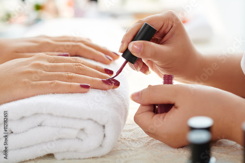 Zdjęcia Side view of manicurist applying marsala nail polish