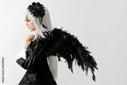 Cosplay girl with white hair , black wings , in a black dress with colored eyes in ryushah and decorations in the studio during the day .