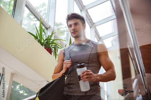 Zdjęcia Sportsman walking and drinking water after training in gym