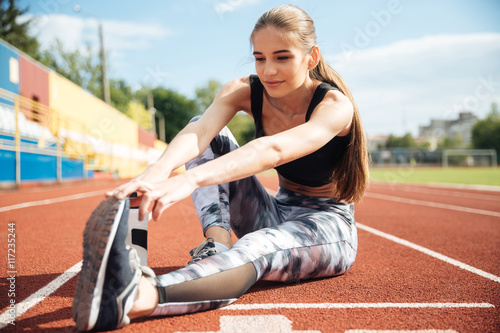 Zdjęcia Woman athlete sitting and stretching legs on stadium