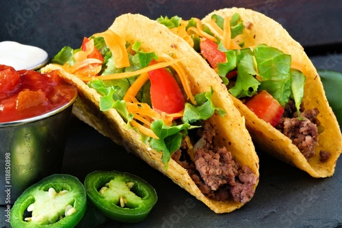Vászonkép Hard shelled tacos with ground beef, lettuce, tomatoes and cheese close up, on s