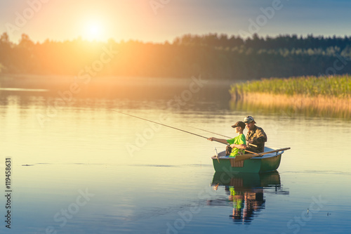 father and son catch fish from a boat at sunset