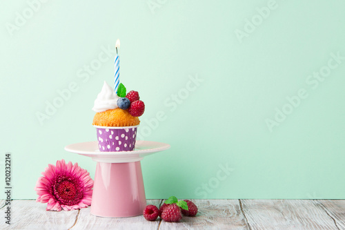 Poster Delicious birthday vanilla cupcake with fresh raspberries, cream and lighted candle on a green mint background, selective focus