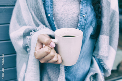 Close up view of woman covered in blanket holding cup of coffee. 