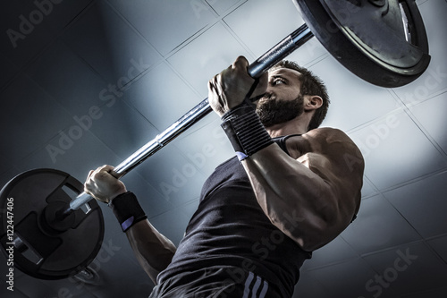 Poster Hombre con grandes músculos levantando peso mientras entrena en el gimnasio