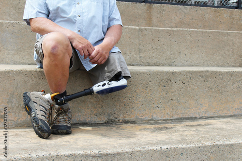 Amputee with legs crossed sitting on concrete bleachers
